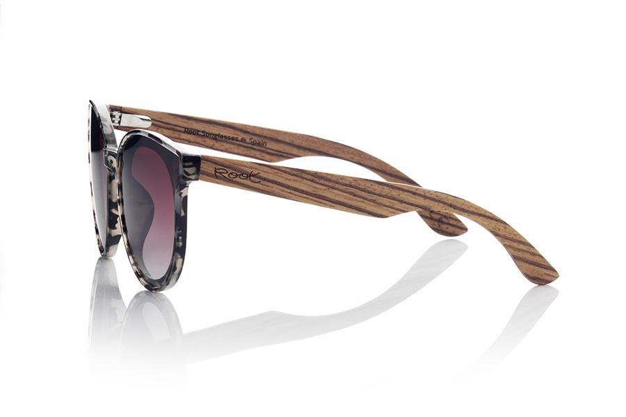 Wood eyewear of Walnut INTHIRA. INTHIRA sunglasses are the perfect complement to any feminine look. Her frontal frame in tortoiseshell shades of black, gray and cream and her rounded shape make her stand out. The lenses are mounted overexposed in the frame, giving it a very modern and attractive look. The wide temples are in grained walnut contrasting with the frame. This model is available in several lens colors, so you can choose the one that best suits your tastes and needs. With INTHIRA sunglasses, you will not go unnoticed. Front measurement approx: 142x55mmApprox front measurement: 142x55mm for Wholesale & Retail | Root Sunglasses® 